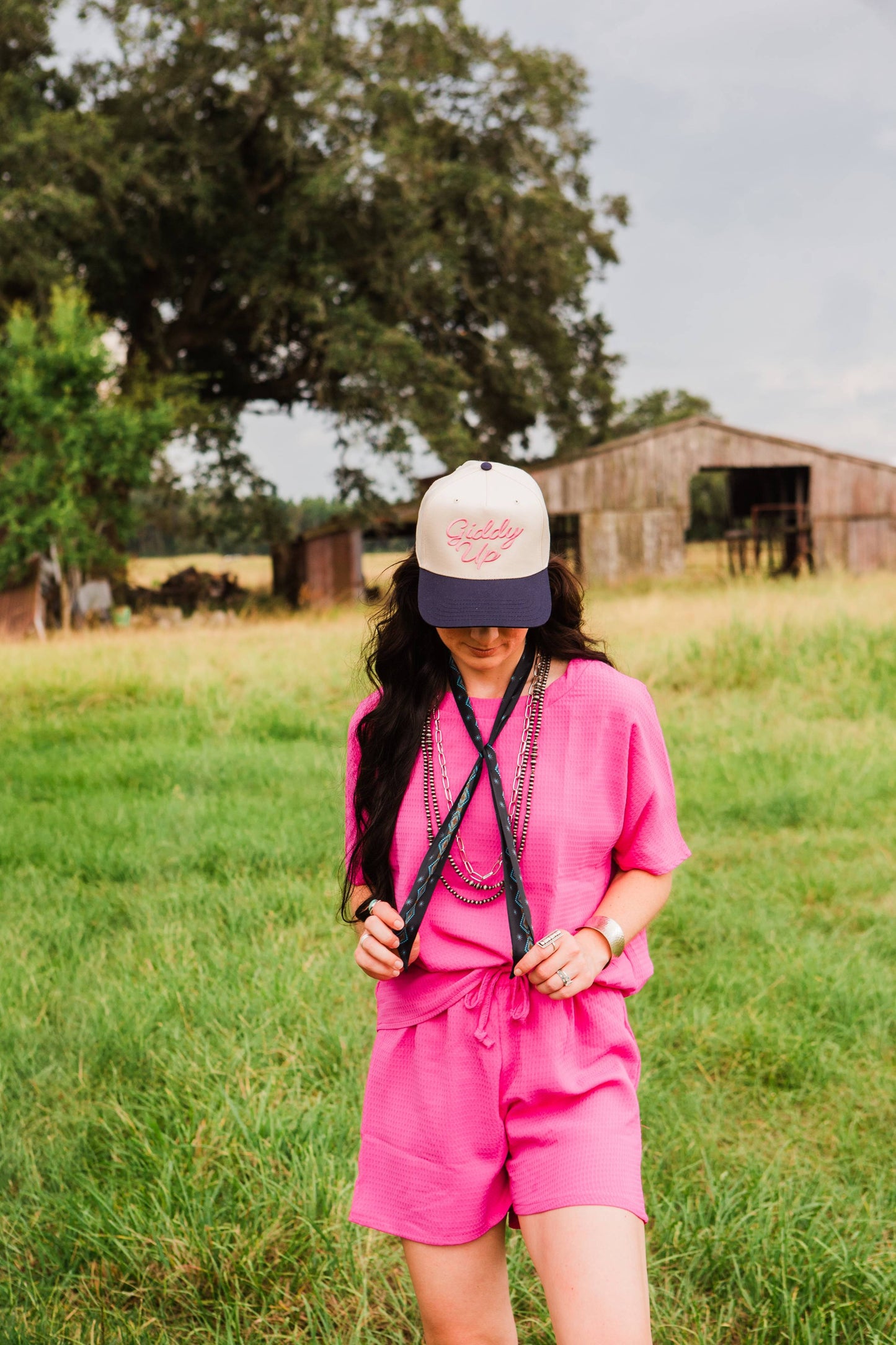 Person wearing a pink outfit and cap in a grassy field with a barn in the background