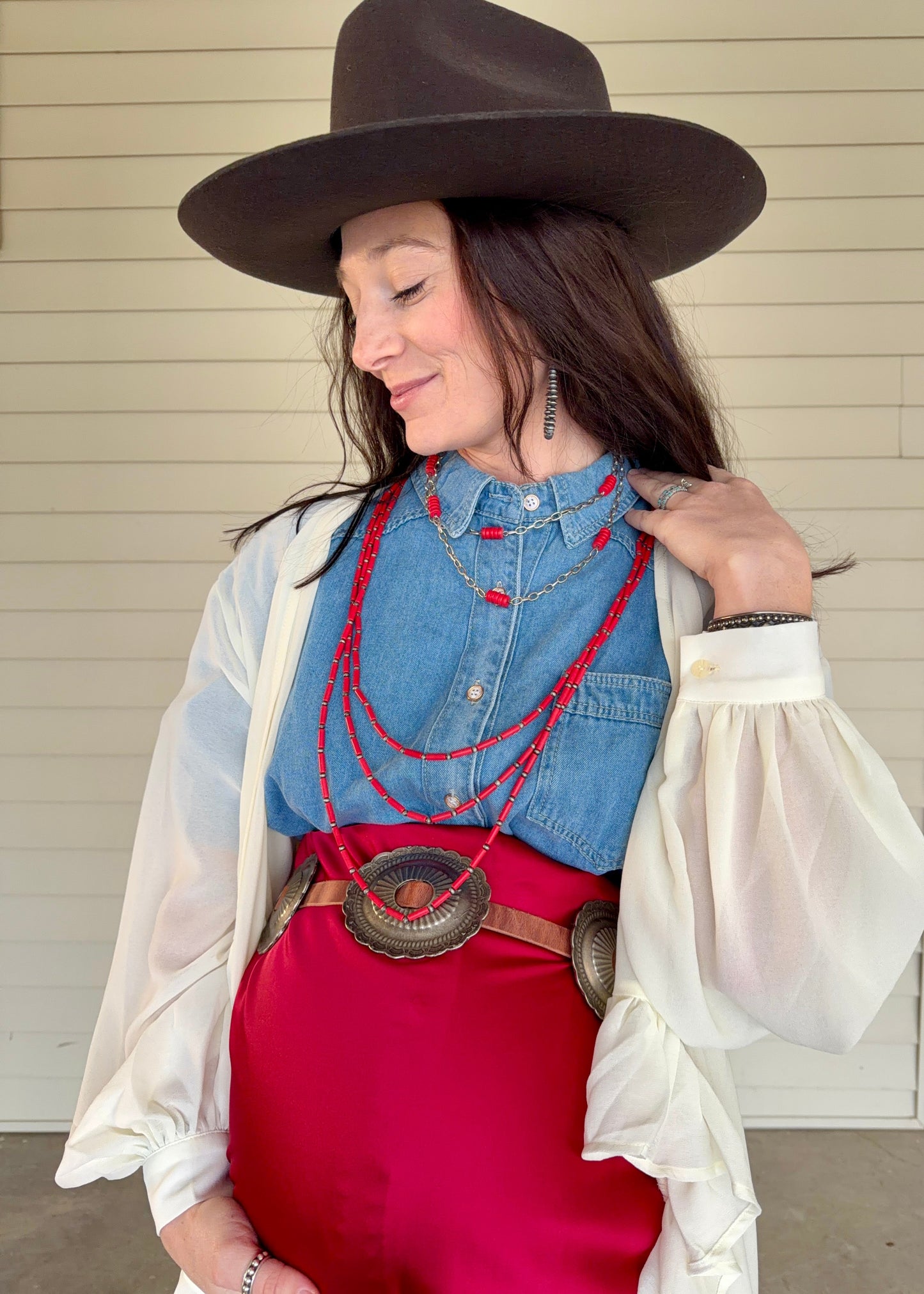Woman wearing a denim top, red skirt, and cowboy hat with a white cardigan.