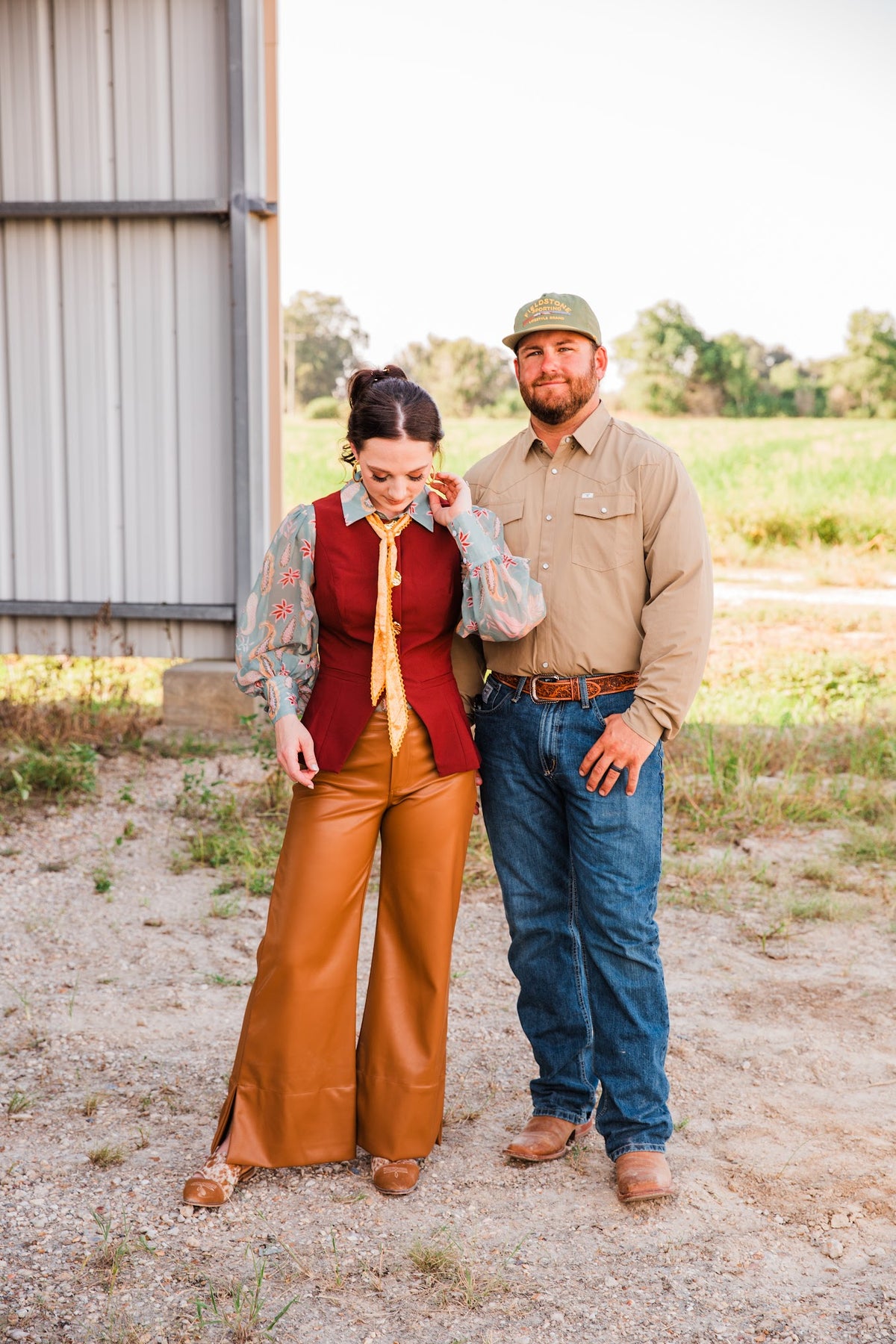 Model wearing the burgundy Carmen Vest over a paisley blouse beside a man in a khaki Western shirt and jeans outdoors.