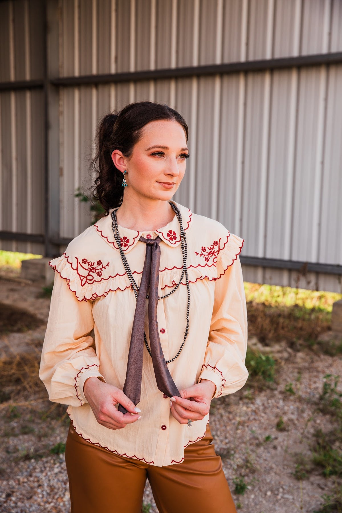 Whisper turquoise dangle earrings on a model wearing a cream floral-embroidered blouse, brown neck tie and caramel pants.