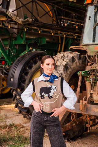 Bull Nettle Knit Vest by 2 Fly Co styled with a white collared blouse, blue neck scarf and washed black jeans beside a tractor.