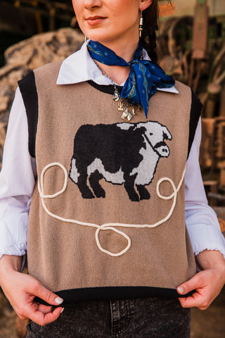 Bull Nettle vest close-up showing tan knit texture, black ribbed armholes and a black and white bull above looping rope detail.