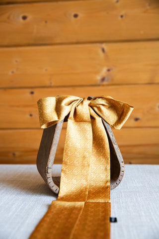 2 Fly Co Fly Hound Twilly in gold, a slim houndstooth scarf tied in a bow on a wooden stirrup with long ends draped forward.