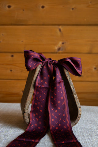 2 Fly Co My Lucky Twilly in Wine with a repeating horseshoe print and narrow striped edges, tied around a rustic stirrup.