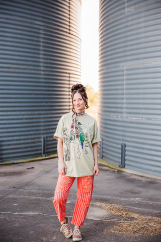 Sadie wearing the Adios graphic tee untucked with orange patterned pants, a printed neck scarf and sneakers.