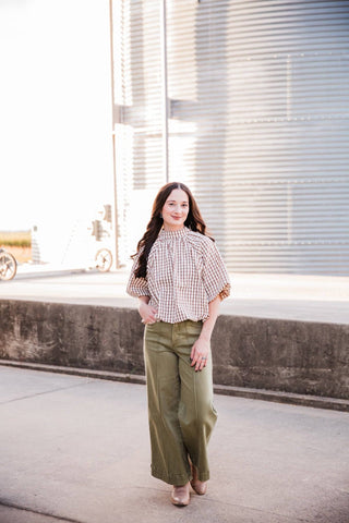 Model walking in the Autumn Ridge Plaid Blouse with olive wide-leg jeans and neutral boots.