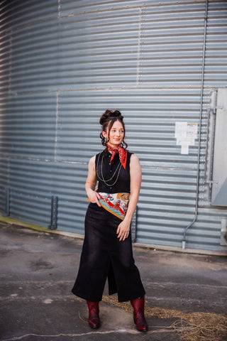 Sadie styling a red Blazing Trails neck bandana with a black sleeveless dress, a printed waist scarf and red Western boots.