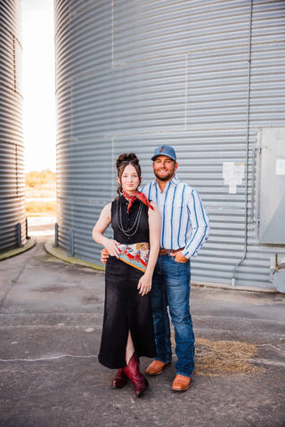 Sadie wearing a red Blazing Trails neck bandana with a black dress and red boots, beside a man in a striped shirt.