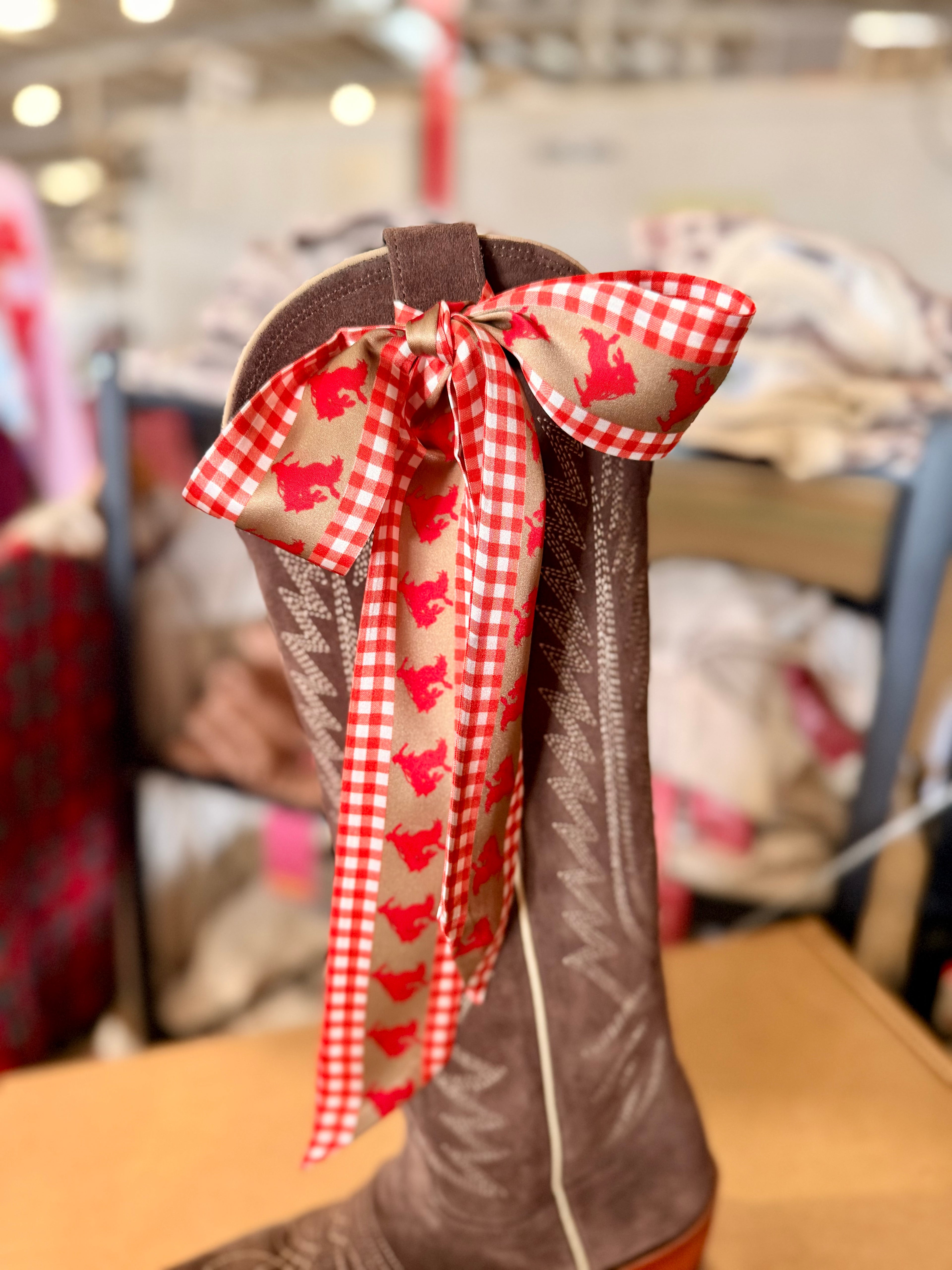 Brown boot with a decorative red and white checkered bow featuring dog patterns in a store setting.