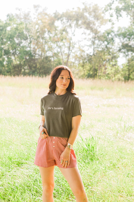 Woman standing in a field wearing an 'He's Farming' t-shirt
