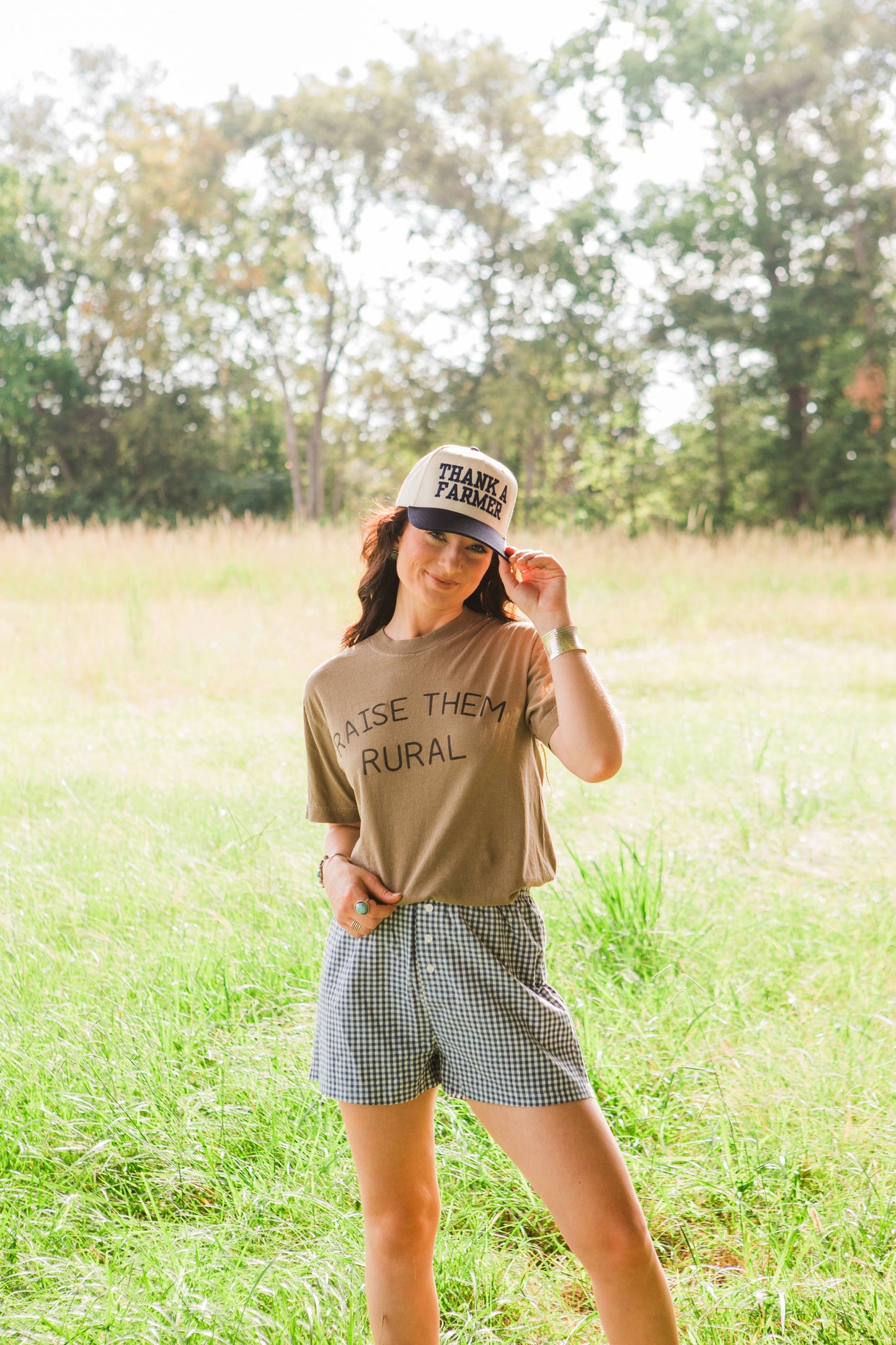 Woman wearing a cap and t-shirt in a field with trees in the background