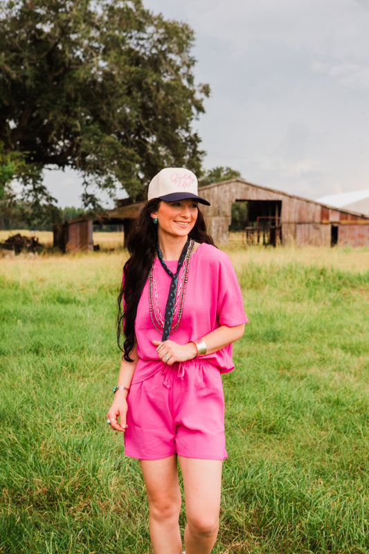 Woman in a pink outfit standing in a grassy field with a barn in the background