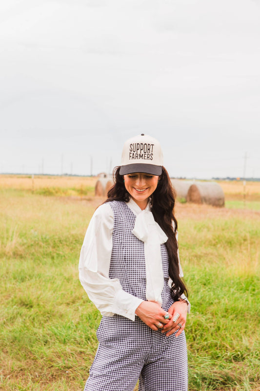 Woman wearing a 'Support Farmers' cap in a field with bales of hay.