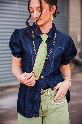 Sadie holding the pointed end of the light green Cowhand Tie, showing its orange motif print against a dark denim top.