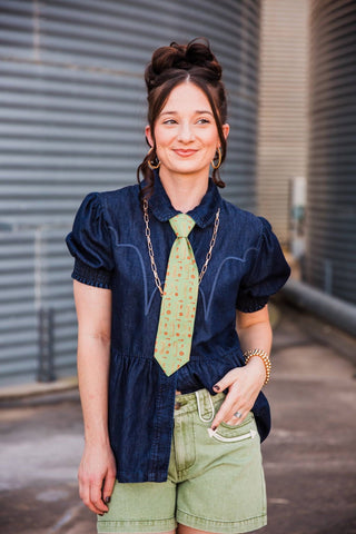 Sadie wearing the light green Cowhand Tie beneath a denim collar, styled with a long chain necklace and green shorts.