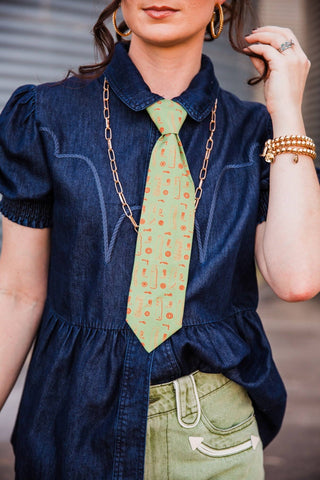 Close-up of the light green Cowhand Tie with small orange Western motifs, knotted beneath a dark denim collar.