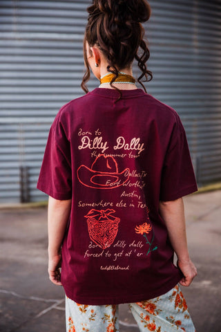 Back of the burgundy Dilly Dally Tee with “Born to Dilly Dally” lettering, Texas tour locations, cowboy hat, bandana and flower.