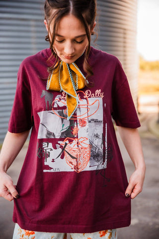 Close-up of the burgundy Dilly Dally Tee’s Western collage graphic with cowboy imagery, a hat outline, bandana and flowers.