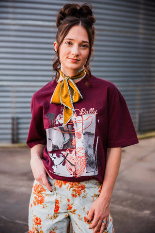 Sadie styling the burgundy Dilly Dally graphic tee tucked into floral pants with a gold neck scarf.