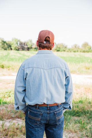 Back view of a light wash denim shirt showing the pointed Western yoke and long sleeves, worn tucked into jeans.