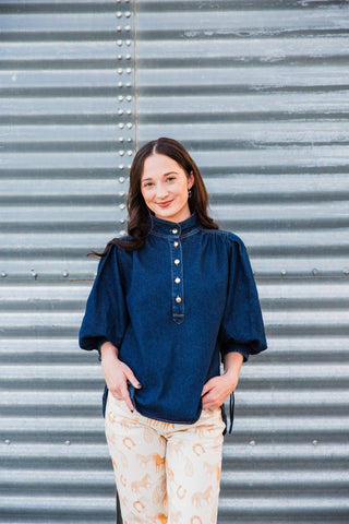 Front view of the dark blue Hadley Denim Top with puff sleeves and a button placket, styled with cream printed pants.