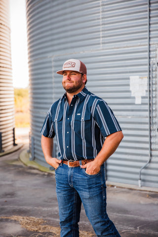 Trevor wearing the navy Hatfield in Blue pearl snap with white vertical stripes, short sleeves, jeans and a leather belt.