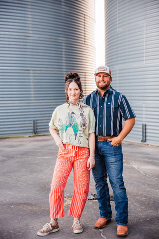 Trevor wearing the striped Hatfield in Blue short-sleeve pearl snap with jeans and brown boots, standing beside Sadie.