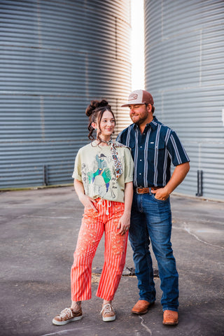 Trevor in the navy-and-white striped Hatfield in Blue pearl snap, posing beside Sadie between metal grain bins.