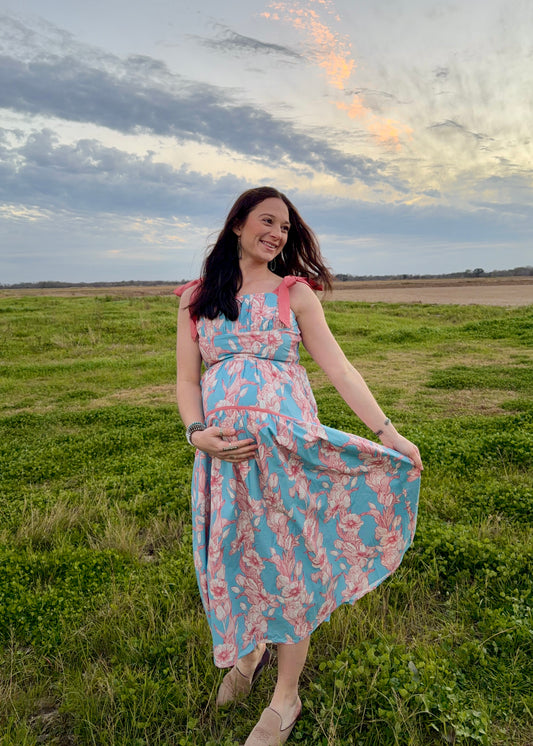 Woman in a floral dress standing in a field with a sunset sky