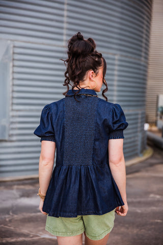 Back view of the dark denim High Roller Top showing a smocked center panel, puff sleeves and a flared gathered hem.