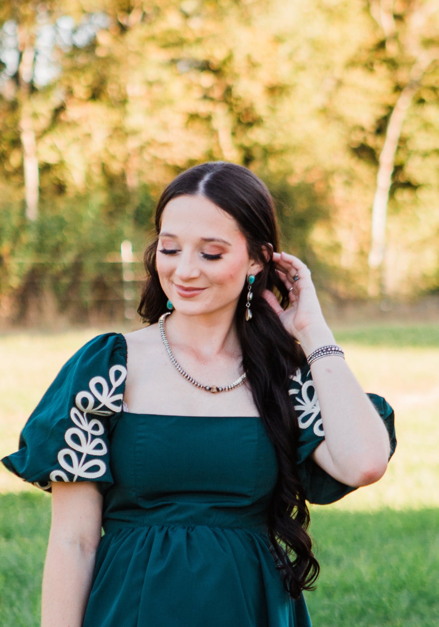 Woman in a green dress with white floral patterns standing in a grassy field.