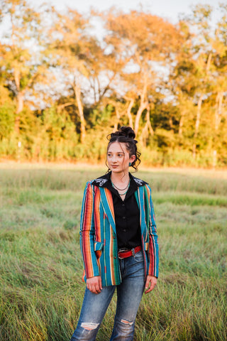 Jade Serape Blazer worn open over a black blouse, showing teal, orange and pink stripes with distressed blue jeans.