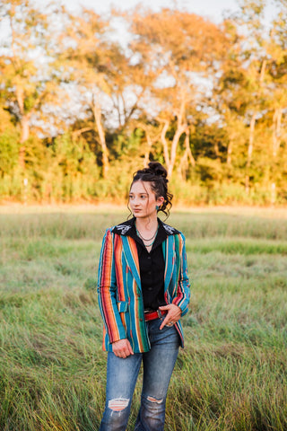 Sadie modeling the Jade Serape Blazer with colorful vertical stripes, long sleeves and flap pockets, styled with denim.