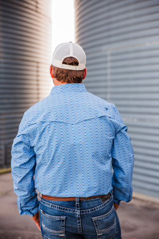 Back view of the blue patterned Jesse pearl snap showing its vented Western yoke and long sleeves, tucked into jeans.