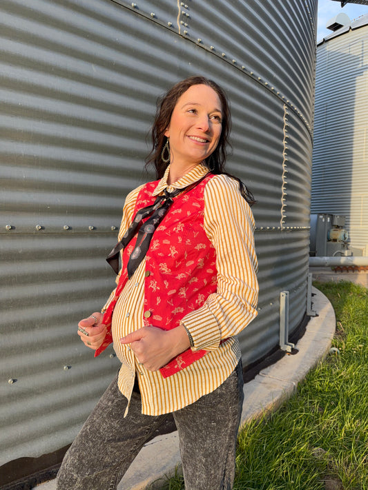 Woman standing in front of rice bins in a red western print vest with a mustard pin stripe long sleeve pearl snap.