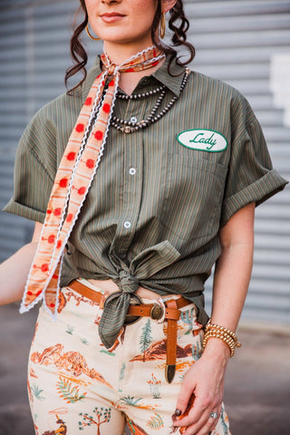 Front detail of the Lady Mechanic top showing olive pinstripes, a Lady chest patch, buttons and a knotted hem.