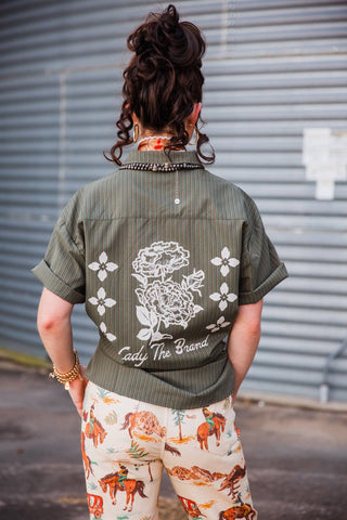 Back view of the olive pinstripe Lady Mechanic top showing white flowers and Lady The Brand lettering.