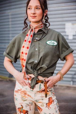 Sadie wearing the olive pinstripe Lady Mechanic top knotted at the waist with Western-print pants and a twilly.