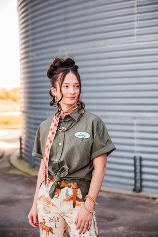Sadie styling the olive Lady Mechanic button-down with a tied front, printed scarf, leather belt and cowboy-print pants.