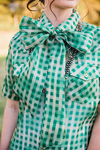 Close-up of the Laurel Gingham Sheer Top showing its green checked bow neckline and buttoned chest pockets.