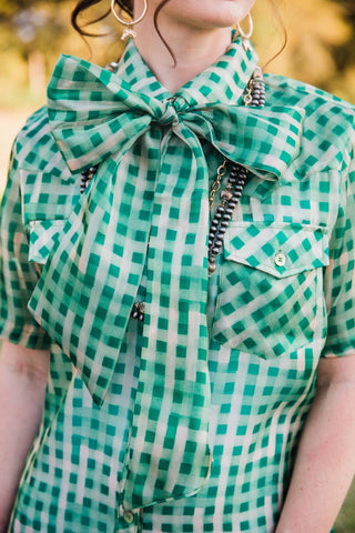 Close-up of the Laurel Gingham Sheer Top's large green gingham bow, button front and chest pockets. lady the brand.