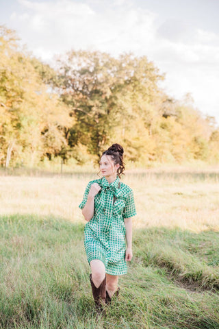 Sadie styling the green Laurel Gingham Sheer Top as a dress with brown cowboy boots outdoors. Lady the Brand