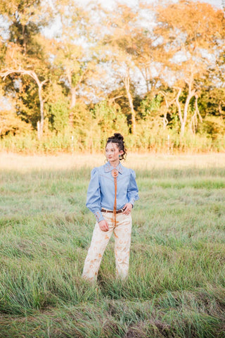 Full outfit view of Sadie wearing Paisley Horse Pants with a blue Western blouse and a bolo-style necklace outdoors.