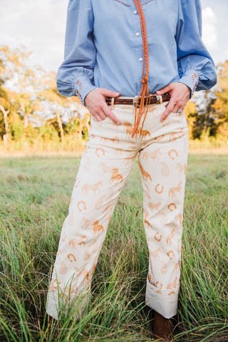 Cream Paisley Horse Pants with warm-toned horse and horseshoe motifs, styled with a blue blouse and brown boots.