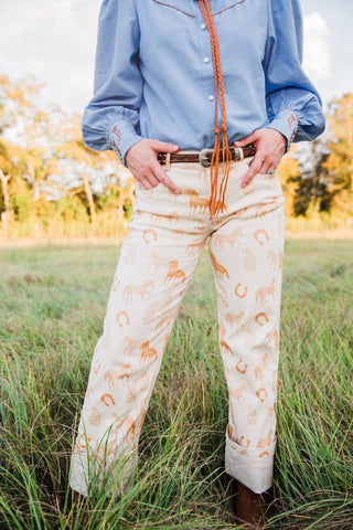 Front view of cream Paisley Horse Pants showing warm-toned horses and horseshoes, straight legs and turned-up hems.