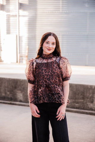 Sable Leopard Blouse worn untucked over black pants, showing the high neckline, short puff sleeves and peplum silhouette.