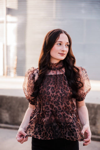 Model holding the Sable Leopard Blouse’s flared peplum hem, showing leopard print, sheer puff sleeves and camisole lining.