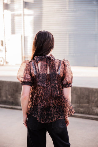Back view of the Sable Leopard Blouse showing a self-tie bow, keyhole opening, sheer puff sleeves and peplum hem.