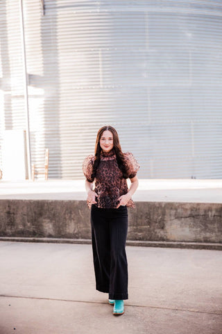 Model walking in the Sable Leopard Blouse, black wide-leg pants and turquoise boots