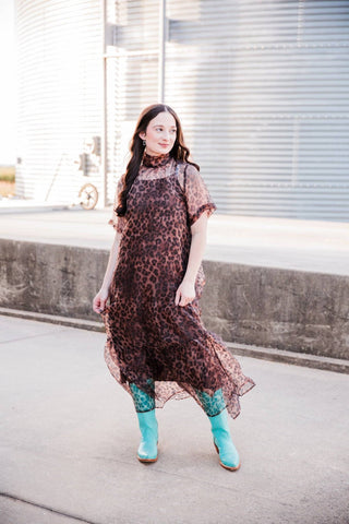 Full-length view of the Sable Leopard Maxi Dress showing its airy silhouette and sheer ruffle hem with turquoise boots.
